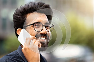 Closeup of happy young eastern man talking on smartphone outdoors