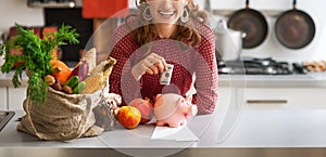 Closeup on happy young housewife putting money into piggy bank