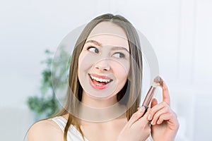 Closeup of happy young woman face with make up brush on light background. Beauty girl skin care concept. Copy space