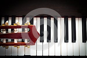 Closeup head of guitar on piano keyboard.