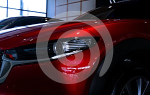 Closeup headlight of shiny red luxury SUV car in showroom. Elegant electric car with sport design. Car parked in showroom. Car