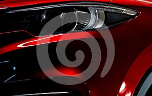 Closeup headlight of shiny red luxury SUV compact car. Elegant electric car technology and business concept. Hybrid auto