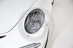 Closeup of the headlight of a white luxury car under the lights against a grey background