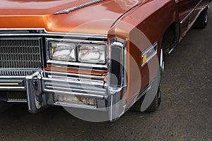 A closeup of the headlights and front bumper on a vintage American automobile. Polished shiny car on a retro exhibition 60-70 year