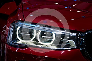 Closeup headlights of modern red car during turn on light in night.