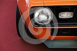 Closeup headlights of an orange retro car.