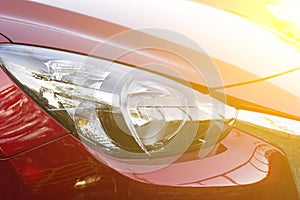 Closeup headlights of red car with sunlight