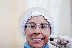 Closeup headshot female nurse wearing bouffant cap and glasses holding up two pill capsules for camera smiling