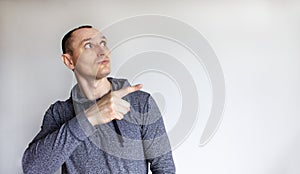 Closeup headshot portrait petrified young handsome man in a grey wear pointing finger to the side, isolated beautiful white