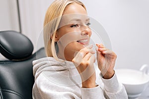 Closeup headshot of pretty young woman patient holding invisible braces aligner during consultation at dentistry clinic