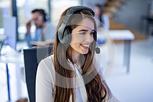 Closeup headshot of smiling young female customer support agent with headset at call center.