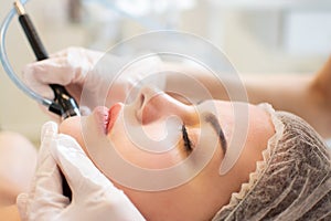 Closeup headshot of young woman receiving hydrafacial therapy at beauty spa.