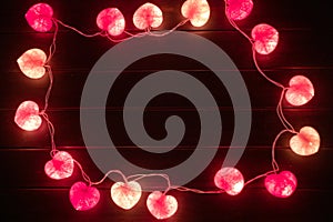 Closeup heart shape of led lights line puts on the wooden table decorated in the darkroom