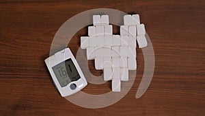 Closeup of heart-shaped refined sugar cubes and a high-blood-sugar glucose meter
