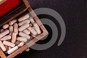 Closeup of herbal capsules filled in an old wooden box with black background and copy space. Ancient medical secrets concept