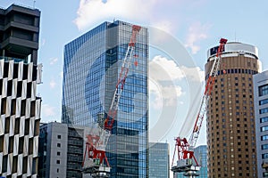Hoisting cranes working on city landscape view and glass office building with blue sky