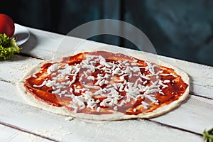 Closeup of a home made raw pizza with cheese and tomato sauce on a wooden background