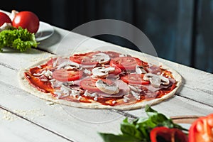 Closeup of a home made raw pizza with cheese and tomato sauce on a wooden background