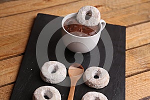 Closeup of homemade bagels, a cup of hot chocolate, and a wooden spoon on a black sheet