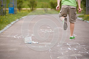 Closeup of hopscotch drawn with chalk on asphalt road and jumping boy. Children games and outdoor activities