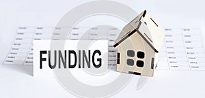 Closeup of house wooden model with blank for text FUNDING . on the chart background