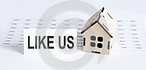 Closeup of house wooden model with blank for text LIKE US on chart background