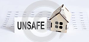 Closeup of house wooden model with blank for text UNSAFE on chart background