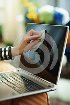 Stylish woman wiping laptop display with cleaning cloth