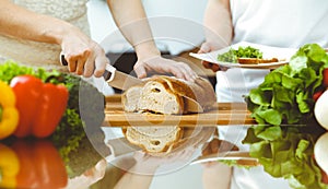 Closeup of human hands cooking in kitchen. Mother and daughter or two female friends cutting bread for dinner