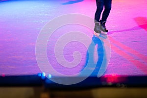 Closeup of human legs in old skates on outdoor public ice rink. Young figure skating on frozen lake in snowy winter park at night