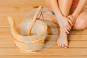 Closeup human woman legs feet and sauna bucket.