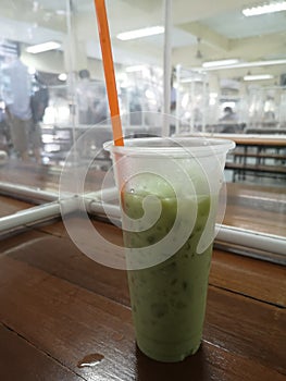 closeup ice green tea in clear plasstic? cup on wooden table in canteen, school cafeteria