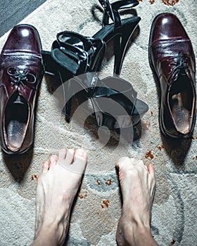 Closeup if man’s bare feet as he chooses to wear men’s shoes or women high heels.