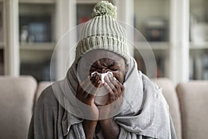 Closeup of ill african american man covered in blanket sneezing