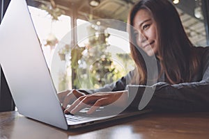 Closeup image of a beautiful Asian business woman looking , working and typing on laptop keyboard with white coffee cup on table