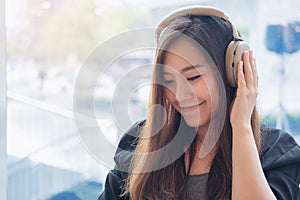 Closeup image of a beautiful Asian woman enjoy listening to music with headphone in modern cafe with feeling relax