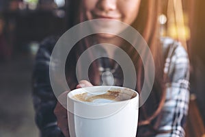 Closeup image of a beautiful Asian woman holding and showing a white mug while drinking hot coffee with feeling good