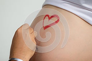 closeup image of beautiful pregnant woman belly with heart painted. Husband paints a heart on his wife's belly.