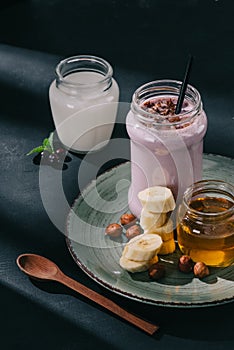 closeup image of berry smoothie, jam, banana slices and walnuts on plate, spoon, yogurt