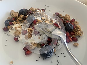 Closeup image of a bowl of organic yoghurt, granola, blueberries, pomegranate arils, chia seeds and honey