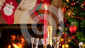 CLoseup image of burning festive candle against fireplace and decorated Christmas tree