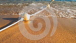Closeup image of calm sea waves rolling and braking on the floating buoys on the sandy sea shore