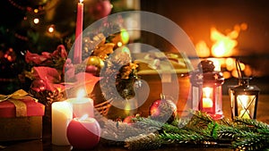 Closeup image of candles and lanterns against Christmas tree and burning fireplace