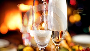 Closeup image of champagne flowing in glasses on romantic dinner at fireplace