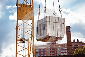 Closeup image of crane lifting heap of bricks at blue sky