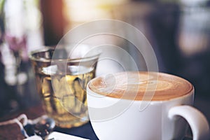 Closeup image of a cup of hot coffee and a tea glass on vintage wooden table