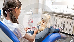 Closeup image of cute girl sitting in dentist chair and playing with her teddy bear in doctor and patient