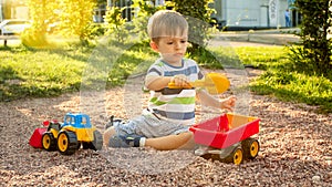 Closeup image of cute little boy playing on the palyground with toys. Child having fun with truck, excavator and trailer