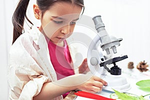 Closeup image of cute little girl working and exploring with microscope. The kid in lab coat learning science in the school