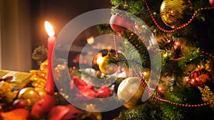 Closeup image of decorated Christmas tree branch against burning candle on traditional wreath